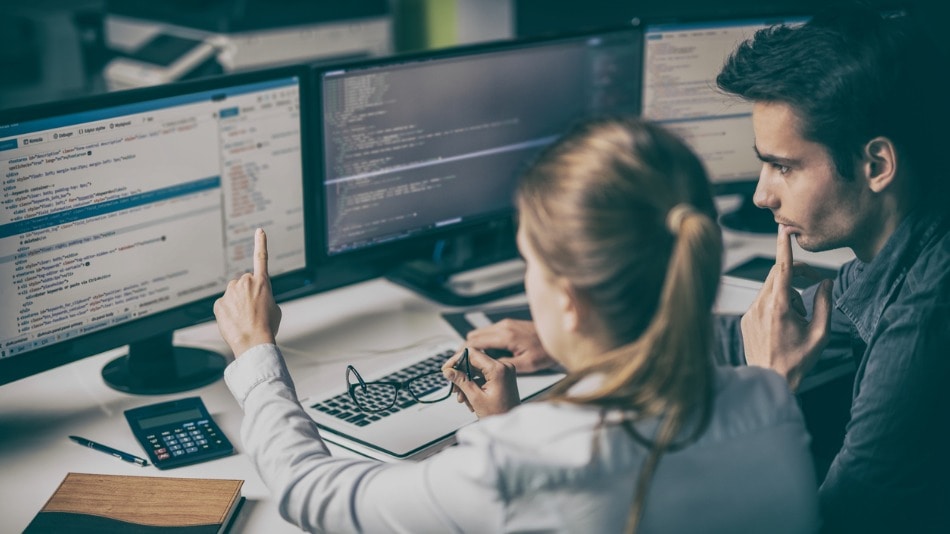Profesionales programando algoritmos en tres monitores en un entorno de desarrollo tecnológico