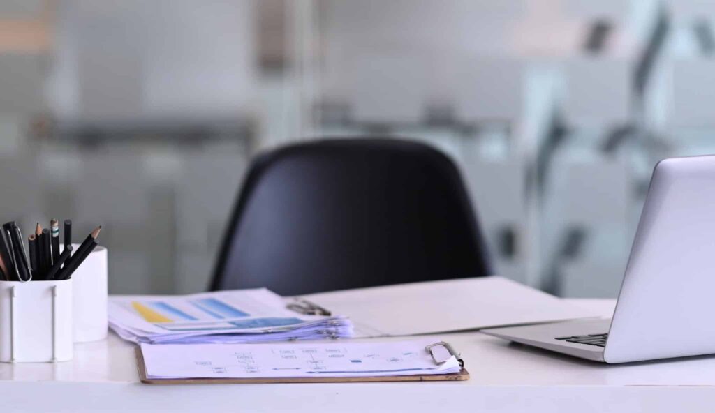 Escritorio de oficina con laptop, documentos y material de trabajo, sin ninguna persona presente, simbolizando absentismo laboral.